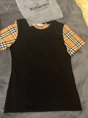 Svart Burberry t-shirt med rutiga ärmar - Säljer min Burberry’s T-shirt fick den i present och den är liten på mig storlek S 