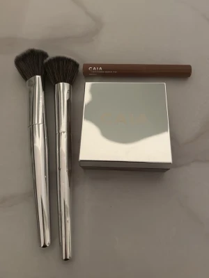 Smink från Caia - oanvänt - Hej! Säljer ett loose setting powder i färgen ”Chocolate Glow” från Caia. Endast testat men inte använt! Nypris: 345kr, Mitt pris: 200kr. Sedan även ett fixing fiber brow gel i färgen ”Brown”, inte ens testat så helt nytt. Nypris: 225kr,  Mitt pris: 120kr. Sedan även två sminkborstar, en foundation borste och en ”cream & liquid brush” F13 & F17 är borstarna. Nypris: 225kr/st. Mitt pris: 100kr/st. Dessa är också testade och finns lite färg på foundation borsten. Pris för allt: 400kr