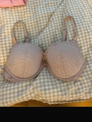 Ljusrosa spets-bh med vaddering - Söt ljusrosa bh med vadderade kupor och spetsdetaljer över hela framsidan. Justerbara axelband och bygel för extra stöd. Liten defekt vid armhålan, sista bild.