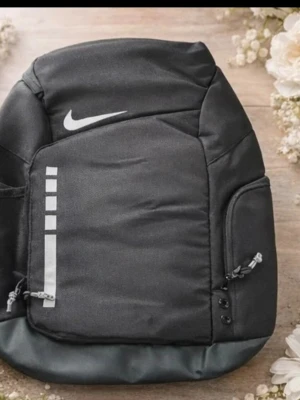 Svart Nike ryggsäck med logga - Snygg svart ryggsäck från Nike med vit logga och reflekterande detaljer. Ryggsäcken har vadderade axelband med Nike-tryck, flera fack med dragkedja och robust botten. Perfekt för skola eller träning och rymmer allt du behöver. Sportig och stilren design.