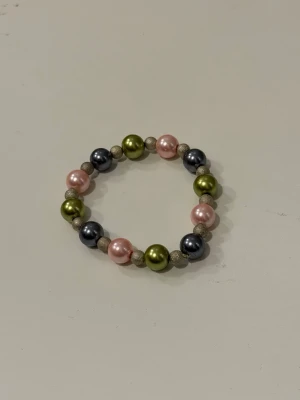 Färgglatt pärlarmband  - Handgjort armband med stora pärlor i metallicfärger: olivgrönt, rosa och mörkgrått. Mellan pärlorna sitter mindre, glittriga guldfärgade kulor. Armbandet är elastiskt.