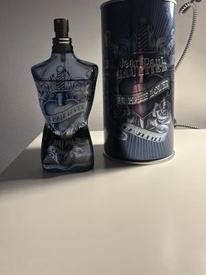 Jean Paul Gaultier Le Male Lover EdP - Jean Paul Gaultier Le Male Lover Eau de Parfum i 125 ml flaska. Flaskan har en unik design i form av en manlig torso i mörkblått glas med silverdetaljer och matchande metallburk. En ikonisk doft med cool och edgy look, perfekt för dig som gillar statement-parfymer. 100ml kvar