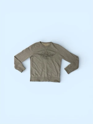 Ralph Lauren tröja  - Grå sweatshirt med tryck framtill från Denim & Supply. Tröjan har rund halsringning, långa ärmar och ribbade muddar vid ärmslut och nederkant. Perfekt för en avslappnad och stilren look. Finns liten defekt vid kragen