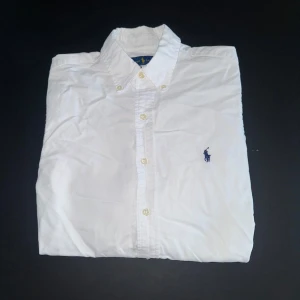 Vit skjorta från Ralph Lauren - Klassisk vit skjorta från Ralph Laurent slim fit med button-down krage och den ikoniska mörkblå broderade loggan på bröstet. Väldigt bra passform. 
