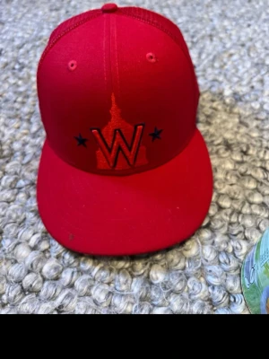 Röd New Era keps med mesh - Snygg röd keps från New Era med mesh på sidorna och bak, samt broderad W-logga och stjärnor framtill. Kepsen har böjd skärm och justerbar snapback. Perfekt för dig som vill sticka ut med en sportig och trendig stil.