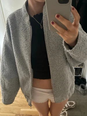 Zara jacka - Mysig grå teddyjacka med dragkedja framtill och avslappnad passform. Jackan har en klassisk rund halsringning och är gjord i fluffigt teddy-material som ger en trendig look. Perfekt för att hålla värmen under kyliga dagar.
