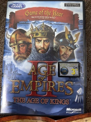 Age of Empires II: The Age of Kings - Age of Empires II: The Age of Kings är ett klassiskt strategispel för PC där du leder en civilisation genom medeltiden. Omslaget är blått med guldtext och visar riddare och slott. Spelet är utvecklat av Ensemble Studios och kommer i en plastfodral. Det finns bara en skiva. Har små repor men fungerar perfekt 