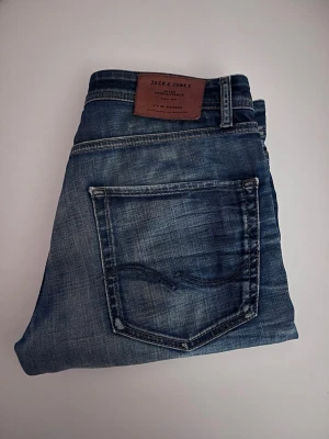 Blå jeans från Jack & Jones - Snygga blå jeans från Jack & Jones med klassisk femficksdesign och slitna detaljer. Jeansen har en normal passform och tydliga tvättade partier för en cool, avslappnad look. Perfekta för dig som gillar en trendig streetstil.