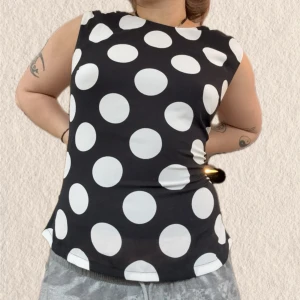 Svart ärmlös topp med vita prickar - Säljer en svart ärmlös topp med stora vita prickar. Toppen har en rak passform och rund halsringning. Perfekt för dig som gillar ett lekfullt och trendigt mönster.