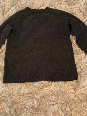 Mörkgrå stickad tröja - En enkel och stilren mörkgrå stickad tröja med rund hals och långa ärmar. Tröjan har ribbstickade muddar vid ärmslut och nederkant. Perfekt för lager på lager och passar till det mesta. Storlek 170, men funkar som en xs-s. Lite nopprig men inget alls som märks. Lambswool blend 