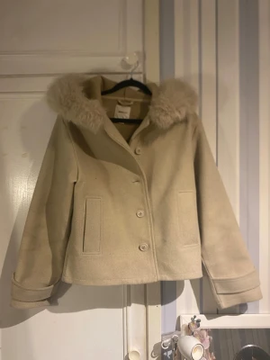 Beige kort kappa med fuskpäls – Gina Tricot (XS) - Superfin beige kappa från Gina Tricot i storlek XS. Klassisk och tidlös modell med mjuk fuskpäls vid kragen som ger en lyxig och feminin känsla. • Kort, rak modell • Knäppning framtill • Dekorativa fickor • Mjuk och skön kvalitet • Perfekt för höst, vår eller mild vinter Väldigt fint skick 🤍 Använd få gånger. Passar lika bra till jeans och sneakers som till klänning och boots för en mer uppklädd look. Säljes då den inte kommer till användning. Kan visa bild på🤍