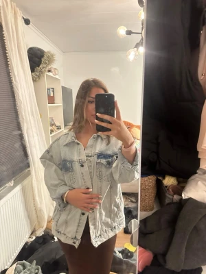 Oversized ljusblå jeansjacka med tryck - Säljer en oversized ljusblå jeansjacka med coolt tryck på ryggen med text. Jackan har klassisk krage, två bröstfickor. Perfekt för dig som vill sticka ut med din stil.