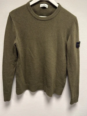 Olivgrön stickad tröja Stone Island - Säljer en olivgrön stickad tröja från Stone Island Junior med klassisk patch på ärmen. Tröjan har rund hals, ribbade muddar och lång ärm. Perfekt för dig som gillar streetwear och vill ha något stilrent men ändå ikoniskt. 100% äkta. Nypris ca 2500-3000kr. Skriv för frågor!