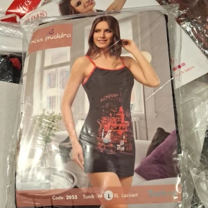 Svart kortklänning med röd print Miss Pudra - Svart kortklänning från Miss Pudra med tunna axelband och röd kontrastkant. Klänningen har ett stort rött grafiskt tryck framtill med stadsmotiv och detaljer. Materialet är mjukt och stretchigt, perfekt för chill eller häng med vänner.