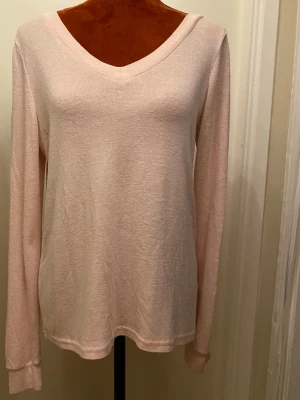 Ljusrosa tröja med V-ringning S - Ljusrosa långärmad tröja med V-ringning både fram och bak. Baksidan har snygga korsade band som detalj. Tröjan är i ett mjukt, tunt material och har en avslappnad passform. Perfekt för dig som gillar stilrena och feminina plagg.