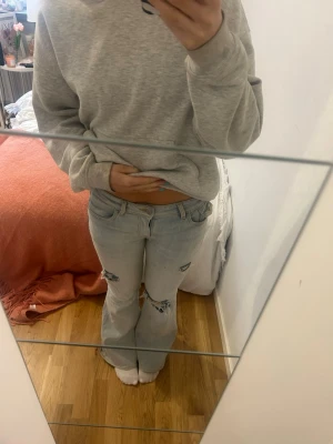 Ljusblå slitna bootcut jeans - Säljer ett par ljusblå bootcut jeans med slitningar och hål på benen. Jeansen har låg midja och en cool detalj med en mörkare bakficka. 