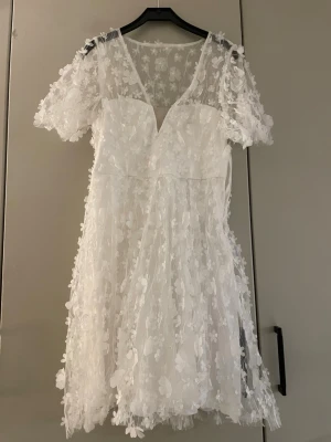 Vit blommig spetsklänning med v-ringning - Superfin vit klänning med korta ärmar och v-ringning. Perfekt till studenten