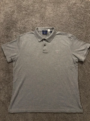 Grå pikétröja från Gant - Snygg grå pikétröja från Gant i regular fit. Tröjan har klassisk krage med två knappar och diskret Gant-logga broderad på bröstet. Tillverkad i mjuk bomull som känns skön mot huden. Perfekt till jeans eller chinos. Piken är i bra skick och har inga defekter. Skriv gärna vid frågor!😃✅