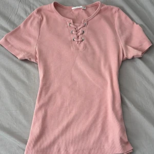 Rosa ribbad topp - Rosa ribbad topp med snörning framtill. Säljer då den inte kommer till användning. Bra skick.
