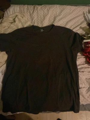 Svart basic t-shirt - En enkel svart t-shirt i klassisk modell med rund hals och korta ärmar. Perfekt till jeans eller shorts för en clean och avslappnad stil. Tillverkad i mjukt material som känns skönt mot huden.