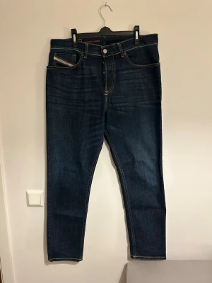 Mörkblå jeans från Diesel - Snygga mörkblå jeans från Diesel med raka ben och klassisk femficksmodell. Jeansen har kontrastsömmar och en liten logga på myntfickan. Tillverkade i ett robust denimtyg som ger en tidlös look. 