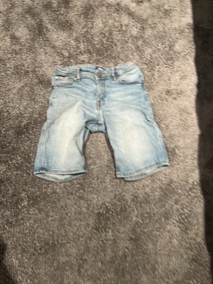 Ljusblå jeansshorts - Säljer ett par ljusblå jeansshorts i klassisk modell. Shortsen har en avslappnad passform och är perfekta för varma dagar. Snygga slitningar och detaljer baktill. Perfekt till sommaren!