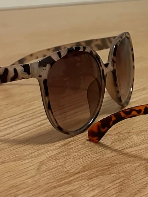 Två solglasögon svart brun leo - Två par solglasögon: 1) Beige-brun leopardmönstrad båge med brunt glas, 2) Organe-brun leopardmönstrad båge med svart glas