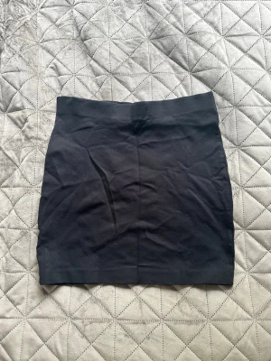 Svart kortkjol från Åhléns - Enkel och stilren svart kortkjol från Åhléns i stretchigt material. Kjolen har en rak passform och är perfekt att matcha med både sneakers och boots. Resår i midjan för extra komfort. Storlek S (36/38).