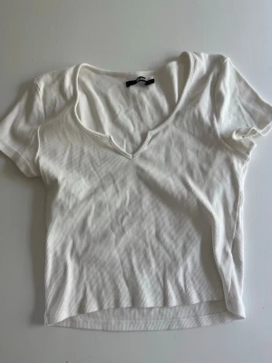 Vit ribbad v-ringad topp - En stilren vit ribbad topp med v-ringning och korta ärmar. Toppen har en figurnära passform och är tillverkad i ett mjukt, stretchigt material som passar perfekt till jeans eller kjol.