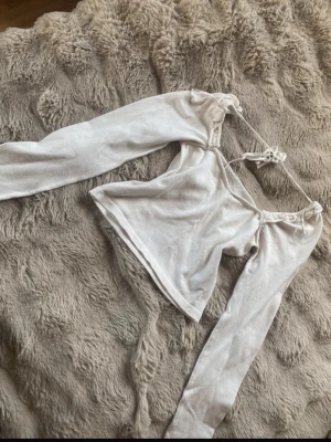 Vit off shoulder topp med knytband - Trendig vit off shoulder topp med långa ärmar och knytband vid axlarna. Toppen har en croppad passform och är gjord i ett mjukt, stretchigt material som ger en snygg siluett. Perfekt för att skapa en cool och avslappnad look. Kanske finns några få fläckar men går bort i tvätten. 