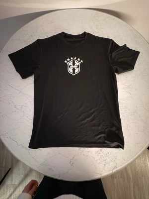 Svart t-shirt från Off-White - Svart t-shirt med Off-White-logga på bröstet. Trycket är vitt och föreställer ett emblem med pilar och stjärnor ovanför. T-shirten har rund hals och korta ärmar, perfekt för en stilren och modern look.