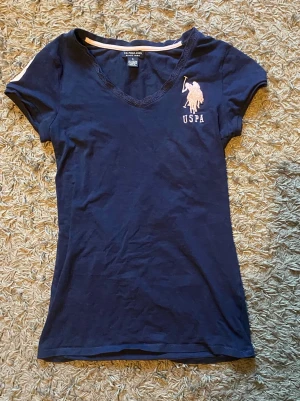 Snygg US.POLO ASSN t-shirt❤️ - Jätte vacker t-shirt med spetts längst öppningen och har färgerna mörk blå och ljus rosa❤️