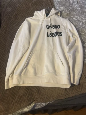 Vit hoodie från Giveno Leônce - Säljer en vit hoodie från Giveno Leônce med svart tryck på bröstet. Hoodien har klassisk känguruficka, dragsko i huvan och ribbade muddar. Perfekt för dig som gillar streetwear och vill ha en clean look.