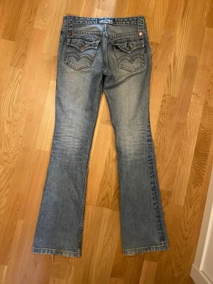 Bootcut jeans från B.T Boy Jeans - Måste tyvärr sälja dessa underbara jeans pga för stor i midjan. Jeansen har jättefina broderade fickor och en jättefin design på bältesbanden som man kan knäppa upp! Dem är lite slitna längst ner på byxbenen, men ingenting man tänker på! Dem är i jättebra längd på mig som är ca 167cm lång, men lite stora i midjan (jag brukar ha storlek 24-23 på jeans). Dem är lågmidjade och bootcut!