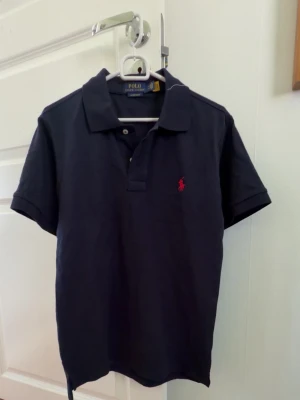 Ralph lauren piké - Absolut inga problem, riktigt snygg till sommaren, mörkblå storlek S. 68cm lång framsida och 71cm baksida.