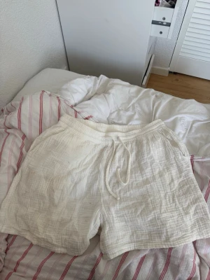 Vita bomullsshorts med snörning - Luftiga vita shorts i bomull med resår i midjan och snörning framtill. De har en avslappnad passform och är perfekta för varma sommardagar. Materialet är mjukt och har en lätt struktur som ger en chill vibe. Kan gå ner i pris om snabb affär 