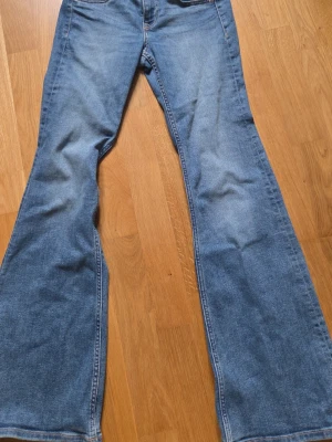 Blå utsvängda jeans med medelhög midja. - Säljer ett par klassiska blå jeans med utsvängda ben och medelhög midja. Jeansen har fem fickor, bälteshällor och stängs med knapp och dragkedja. Perfekta för dig som gillar retrostil och vill ha en snygg siluett.