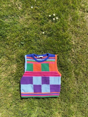 Färgglad stickad linnetopp - Säljer en unik och färgglad stickad linnetopp med rutigt mönster i lila, blått, grönt, orange och rosa. Toppen är croppad och ärmlös med ribbade kanter i flera färger. Så nice nu inför försommaren 🌺🌞 