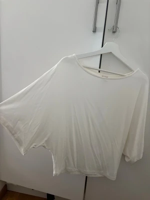 Vit poncho topp med vida ärmar - Säljer en vit poncho topp med vida, lösa ärmar och rund halsringning. Toppen har en avslappnad passform och är tillverkad i ett mjukt, tunt material som känns skönt mot huden. Perfekt för en chill och stilren look.