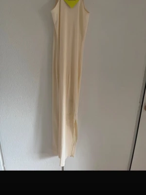 Lång ljusbeige klänning med smala axelband - En stilren lång klänning i ljusbeige med smala axelband och rak passform. Perfekt för varma dagar och enkel att styla med accessoarer. Materialet känns lätt och luftigt.