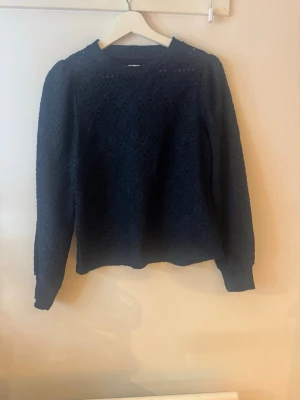 Mörkblå tröja med mönster - Mysig mörkblå tröja med diskret diamantmönster över hela plagget. Tröjan har rund halsringning, långa ärmar och ribbade muddar vid ärmslut och nederkant. Perfekt och enkel att matcha med jeans eller kjol.