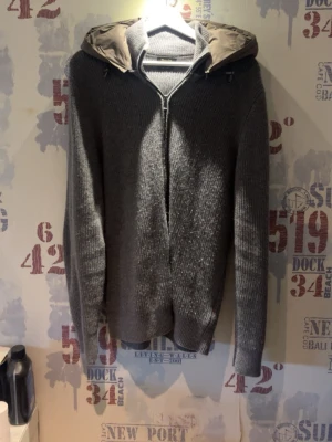 Grå stickad cardigan från Massimo Dutti - Snygg grå stickad cardigan  från Massimo Dutti i extrafin ull. Tröjan har dragkedja framtill, huva med dragsko och ribbade muddar. Perfekt för dig som gillar en stilren och bekväm look.