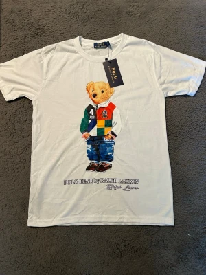 Vit Polo Bear t-shirt  - Vit t-shirt med ikoniskt Polo Bear-tryck framtill. Klassisk rund hals och korta ärmar. Perfekt för dig som gillar streetstyle och preppy vibes.