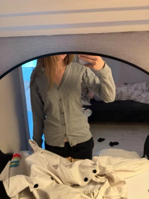 Grå kofta från H&M med knappar - Snygg grå kofta från H&M med knäppning framtill och ribbade muddar. Perfekt att slänga över en t-shirt eller linne. Enkel och stilren design som passar till det mesta. Stor i storleken