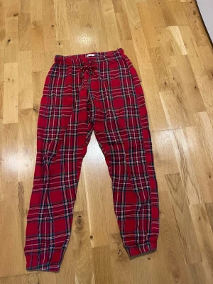 Cubus Rödrutiga pyjamasbyxor med dragsko stl S - Cubus Snygga pyjamasbyxor i rött med klassiskt rutigt mönster i vitt, svart och grönt. Byxorna har resår och dragsko i midjan för skön passform samt muddar vid bensluten. Perfekta för mysiga hemmakvällar.