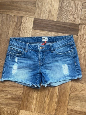 Blå jeansshorts från ONLY med slitningar - Snygga blå jeansshorts från ONLY med slitna detaljer och fransig kant nedtill. Klassisk femficksmodell med knapp och dragkedja framtill. Perfekta för varma dagar och en avslappnad stil. Kan diskutera pris💗