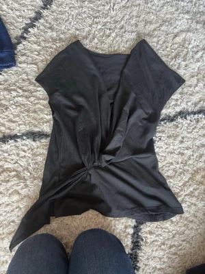 Svart omlottopp från SHEIN - Svart omlottopp från SHEIN i mjukt polyestermaterial med elastan för extra stretch. Toppen har ärmlös design och en snygg knytning i sidan som ger en cool twist till outfiten. Perfekt att styla med jeans eller kjol för en trendig look. den är i storlek S men skulle säga att den den skulle passa M/L också 