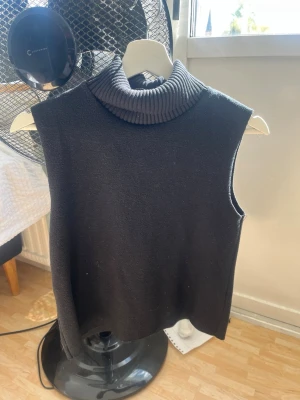 Svart ärmlös polotröja - Svart stickad ärmlös polotröja med bred ribbad krage. Perfekt att styla över en skjorta eller långärmad topp. Mjuk och skön kvalitet, rak passform och minimalistisk design.