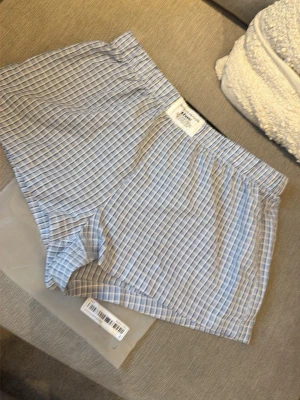 Nya i förpackning! Blårandiga shorts från Ezwear - Säljer ett par shorts från Ezwear med blå och vita ränder. De har en klassisk passform med resår i midjan och är tillverkade i ett lätt och mjukt material, perfekt för vardagskomfort. Snygg och enkel design med etikett framtill.