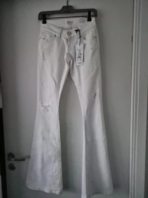 Vita utsvängda jeans - Snygga vita jeans med utsvängda ben. Modellen är low rise och har slitna detaljer på låren och knäna. Klassisk femficksdesign och bälteshällor.